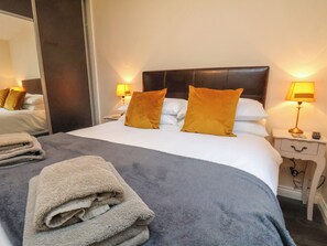A neatly made bed with a grey blanket and two orange pillows, a bedside lamp, and a folded towel on the floor.