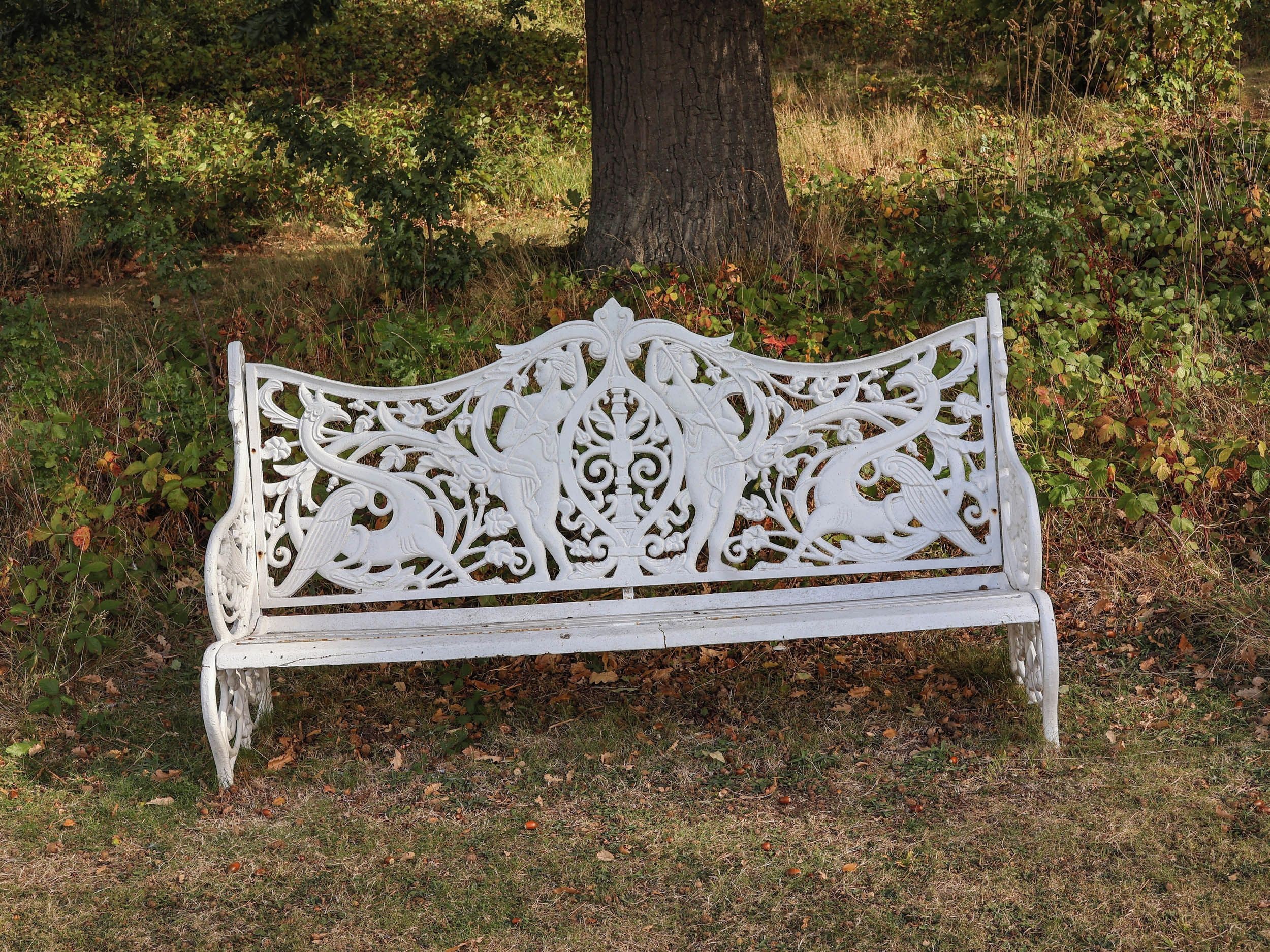 Un banc blanc orné de sculptures complexes, placé dans un espace verdoyant, avec des arbres et une végétation luxuriante en arrière-plan.