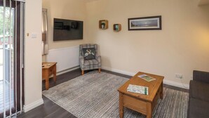 A living room with a grey armchair, a wooden coffee table, a large flat-screen TV, and a framed picture on the wall. - Cowslip (Saltburn-by-the-Sea)