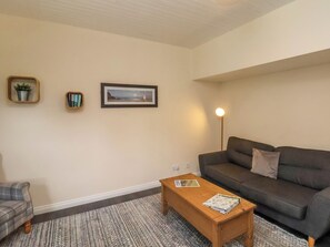 A living room with a grey sofa, a wooden coffee table, a patterned rug, a framed picture on the wall, and a floor lamp. - Cowslip (Saltburn-by-the-Sea)