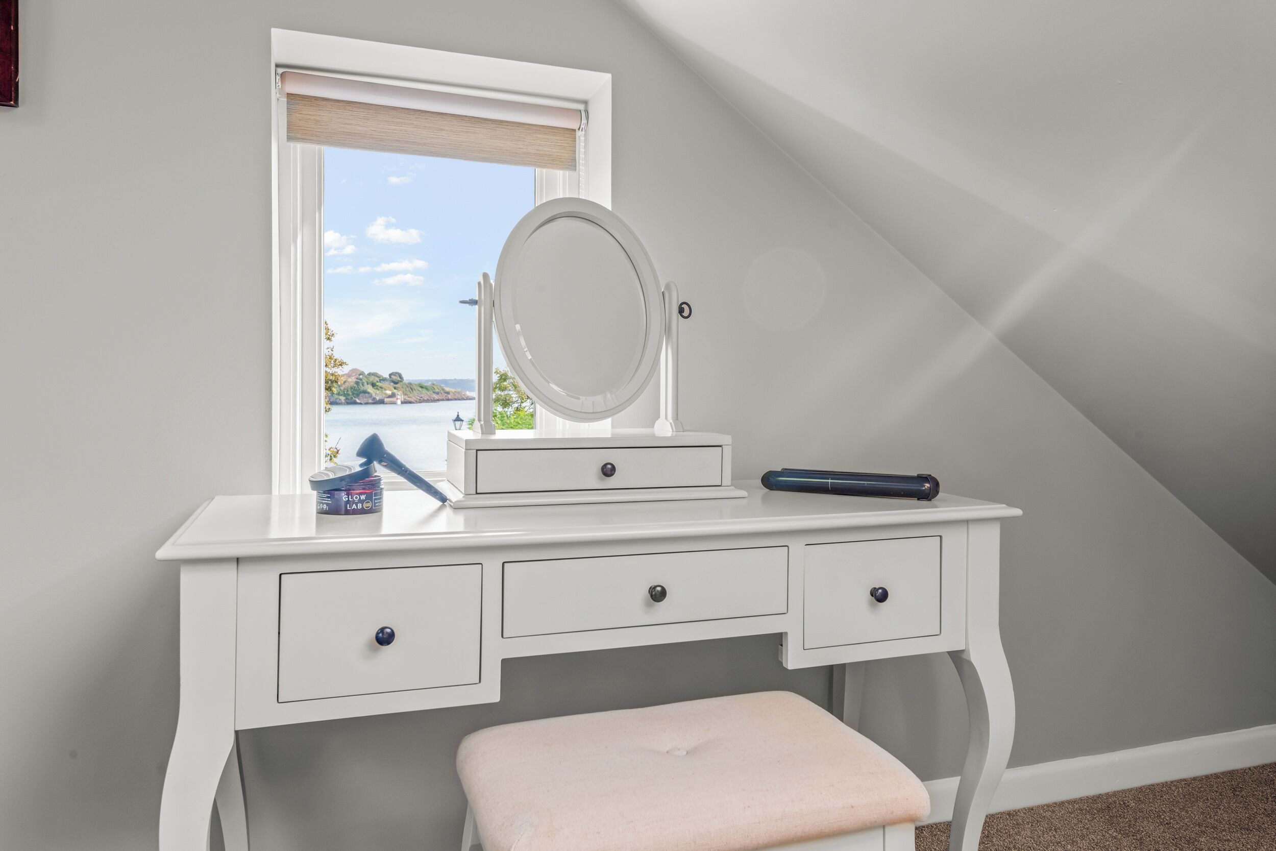 Une coiffeuse blanche avec un miroir, des tiroirs et un banc.