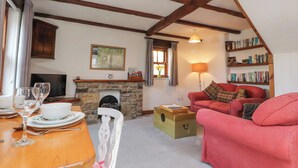 A cozy living room with a stone fireplace, a red sofa, a wooden table with wine glasses, and a bookshelf filled with books. - Mallards Nest (Skipton)