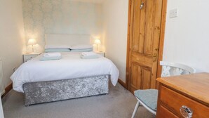 A neatly arranged bedroom with a bed, bedside lamps, a wooden wardrobe, and a chair. - Mallards Nest (Skipton)