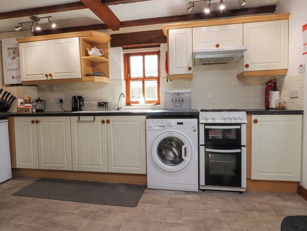 A kitchen with white cabinets, a washing machine, an oven, and a window.