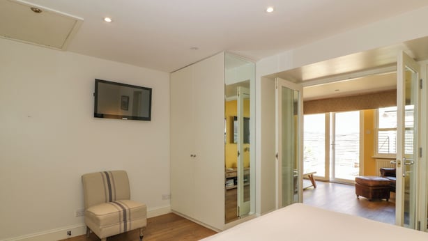 A bedroom with a bed, a chair, a wardrobe, and a television on the wall. - The Suite (Thornhill)