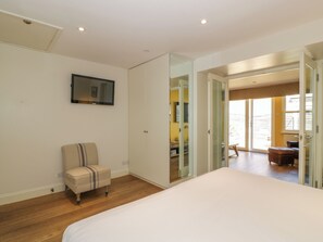 Een slaapkamer met een bed, een stoel, een kledingkast en een televisie aan de muur.