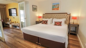 A bedroom with a large bed, two bedside tables with lamps, a dresser, a mirror, and a door leading to another room. - The Suite (Thornhill)