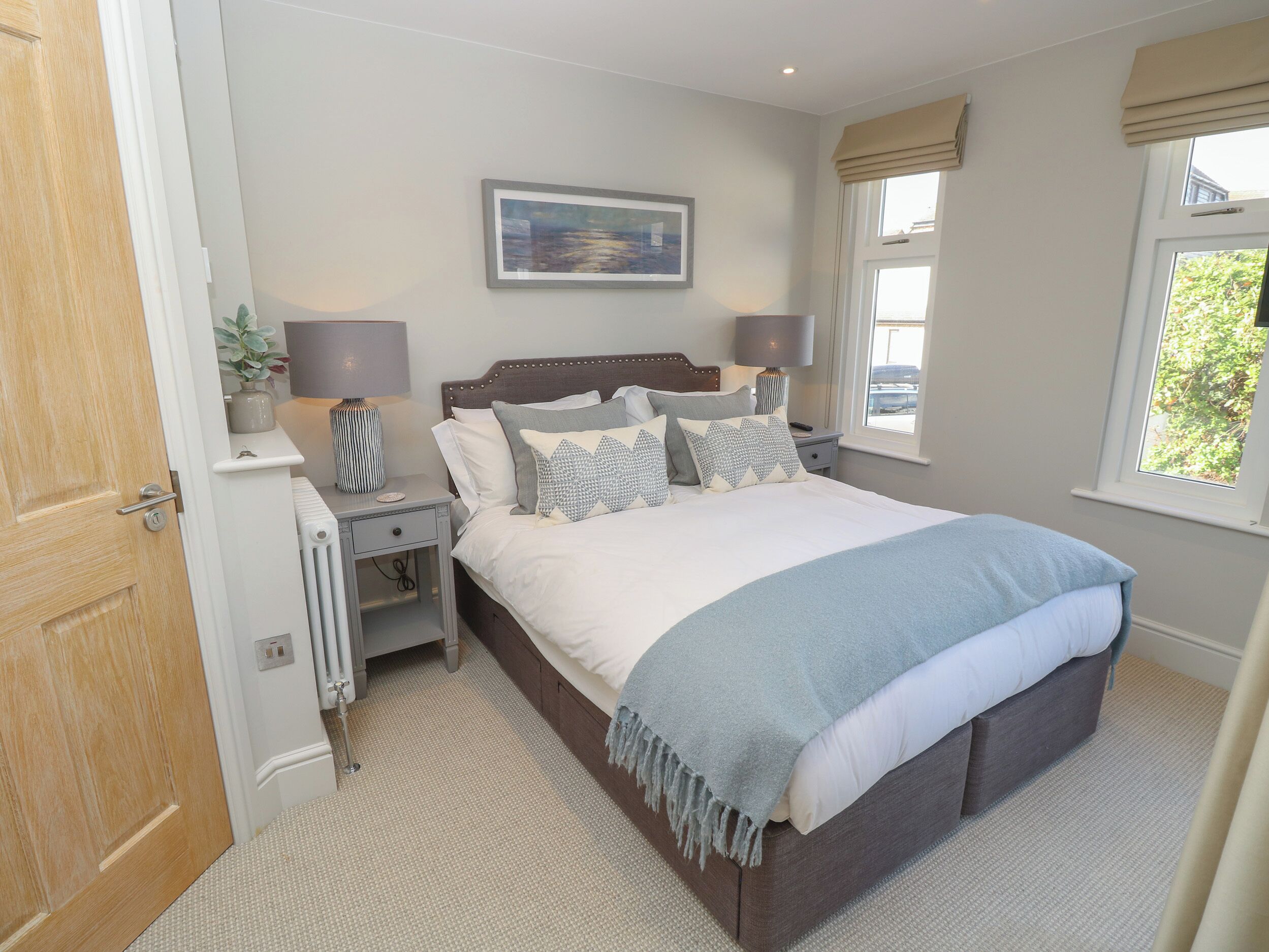 A bedroom with a large bed, bedside lamps, a nightstand, a radiator, and a window with curtains.