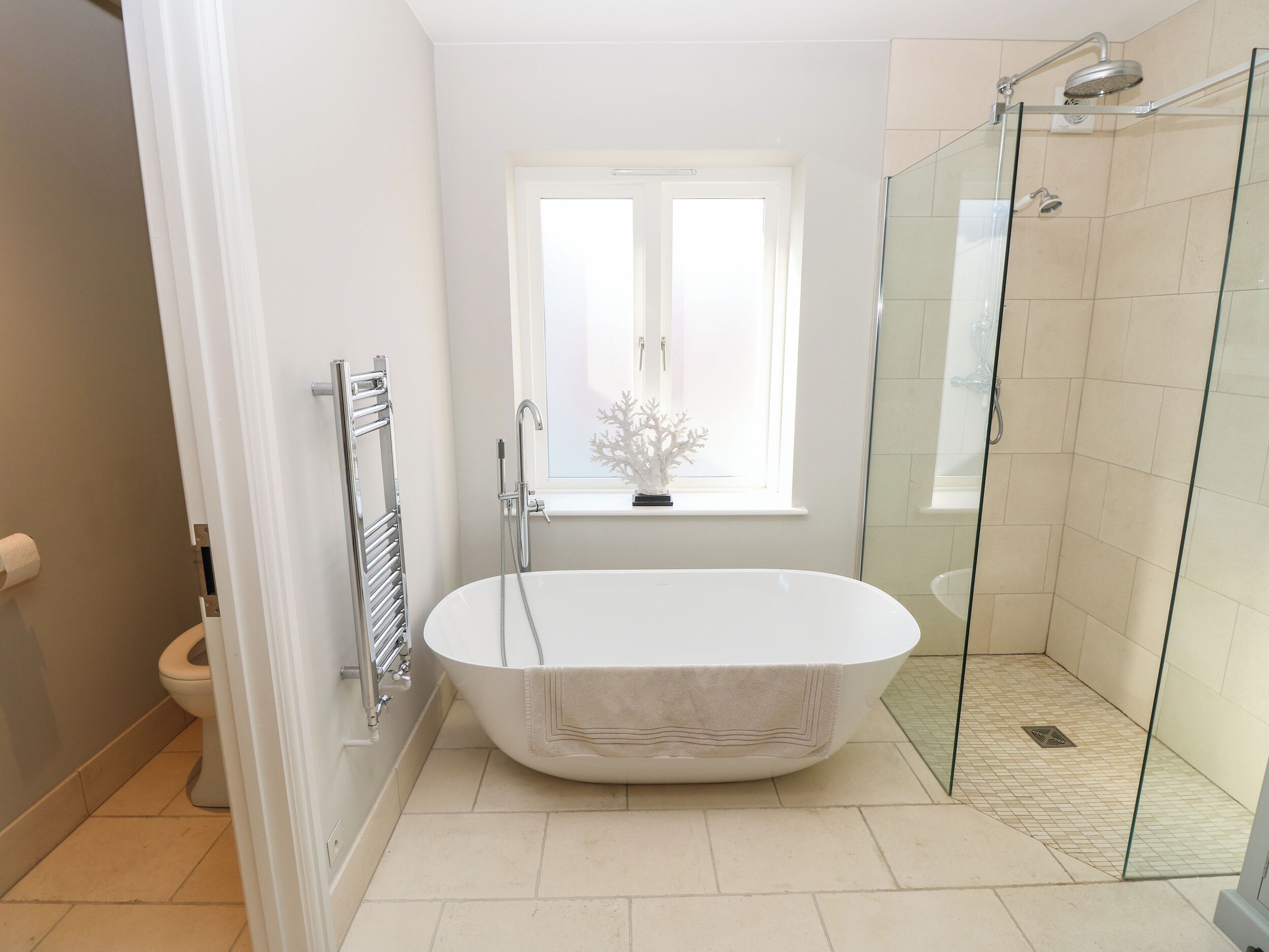A modern bathroom with a freestanding bathtub, a glass shower enclosure, and a window above the sink.