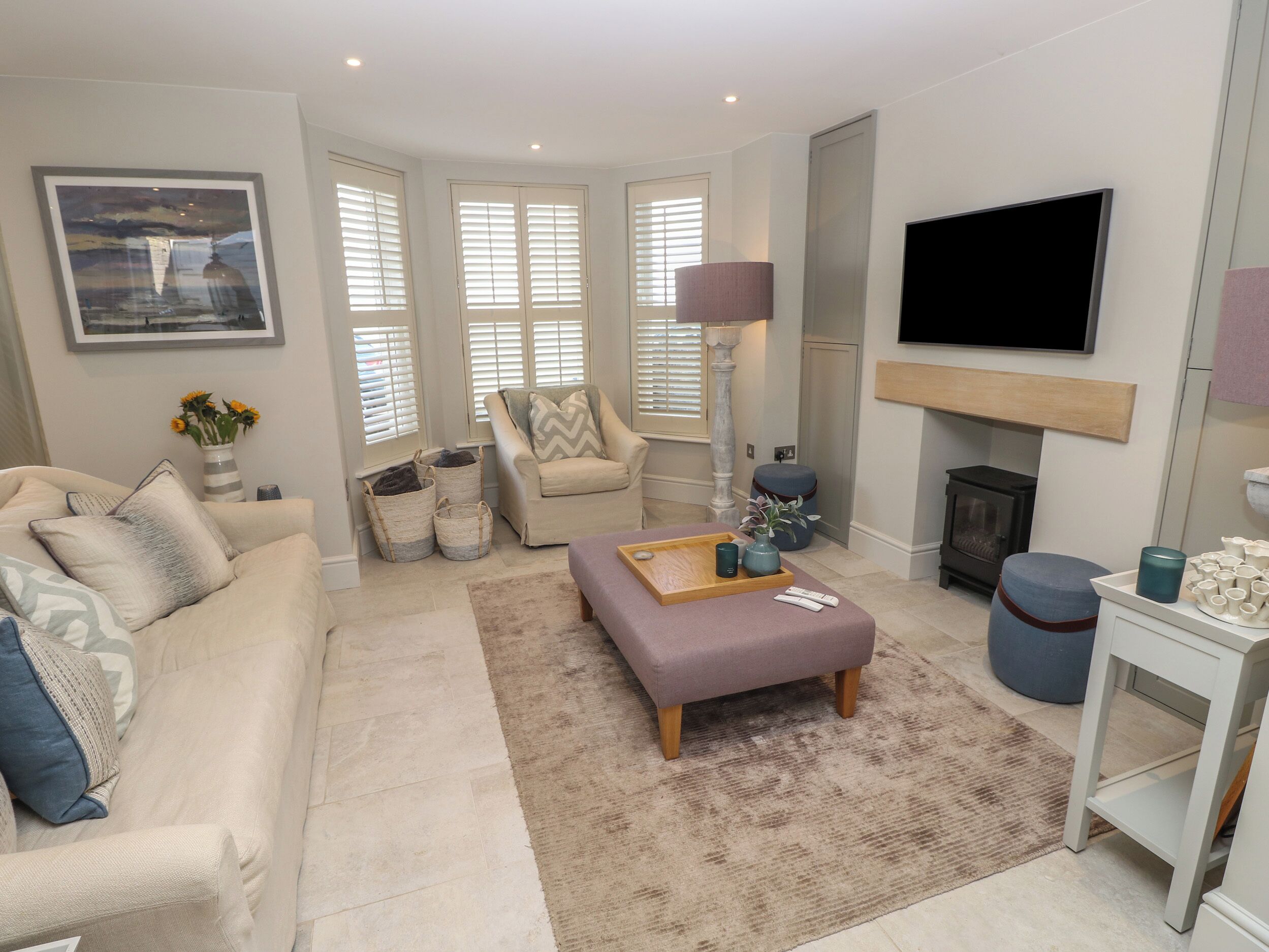 Un salon comprenant un canapé, un fauteuil, un pouf et un téléviseur à écran plat fixé au mur.