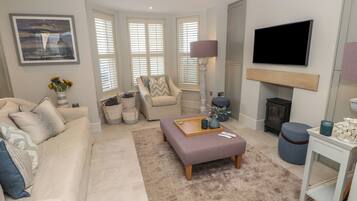 Un salon comprenant un canapé, un fauteuil, un pouf et un téléviseur à écran plat fixé au mur.