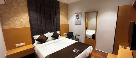 A modern hotel room with a large bed, a desk, a chair, and a mirror.