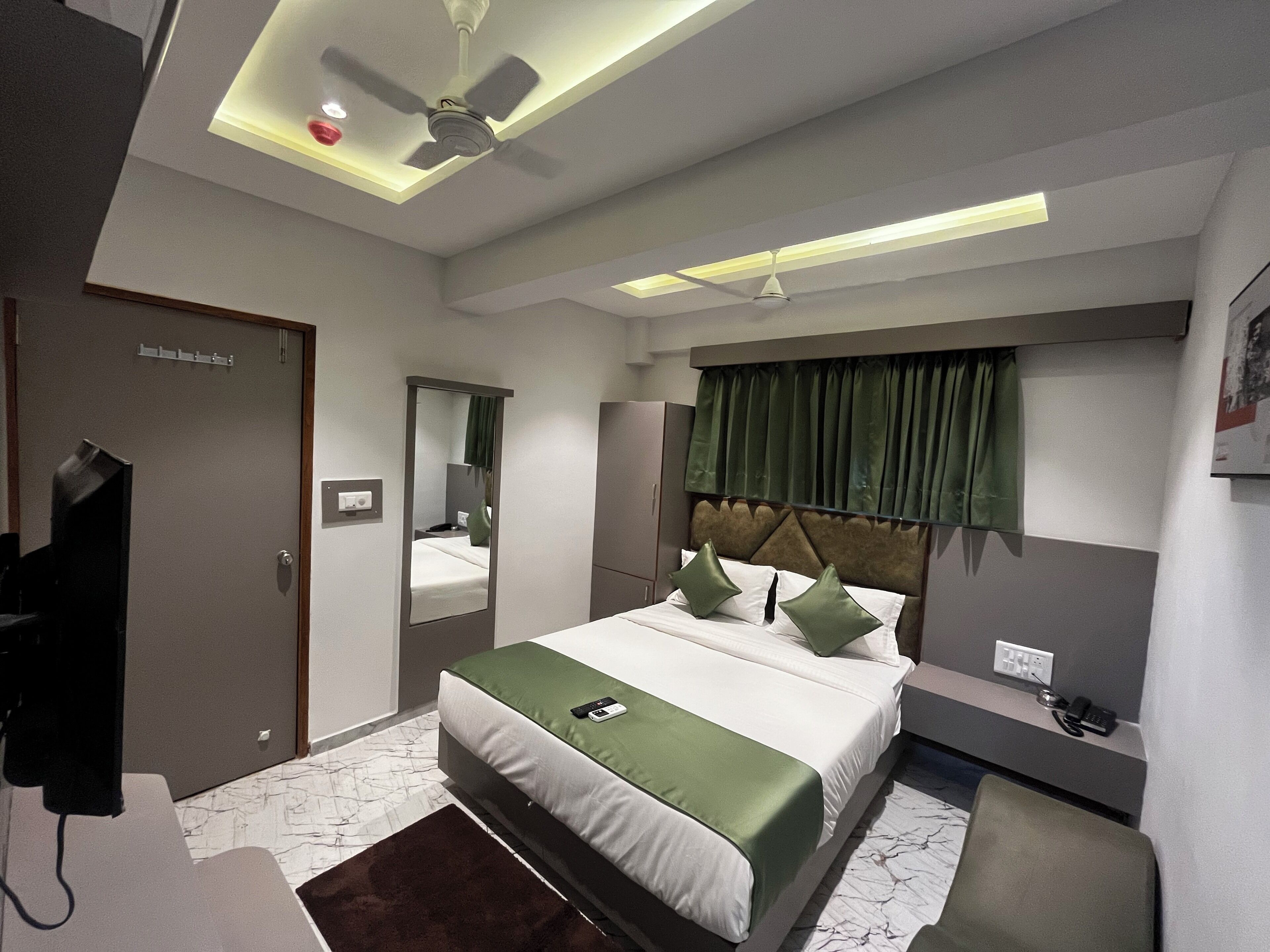 A modern hotel room with a bed, a desk, a chair, a mirror, a ceiling fan, and a window with curtains.