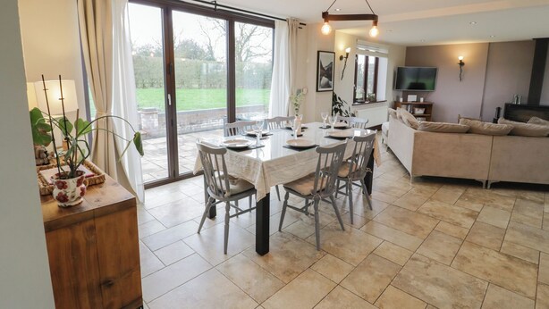 A spacious dining area with a large table, chairs, and a view through glass doors to a garden.