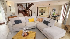 A living room with a beige sectional sofa, a wooden coffee table, and a staircase leading to an upper floor.