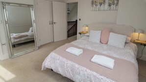 A bedroom with a large bed, a mirror, a painting, and a staircase.
