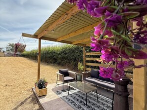An outdoor seating area with a pergola, a sofa, a table, and potted plants. - Little Acre (Evesham)