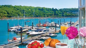 Een jachthaven met boten, een ontbijttafel met croissants, aardbeien, koffie en een glas sinaasappelsap.