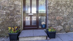 Un bâtiment en pierre avec une porte en bois sombre portant l’inscription « Grenier à foin ». Deux jardinières sont placées devant la porte.