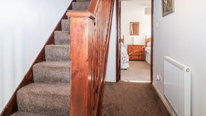 Un escalier dont les marches sont recouvertes de moquette et dont les rampes sont en bois, menant à une chambre où se trouvent une commode et un miroir mural.