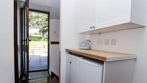 A compact kitchen with a built-in dishwasher, a wooden countertop, and a white cabinet above. - The Dairy (Liskeard)