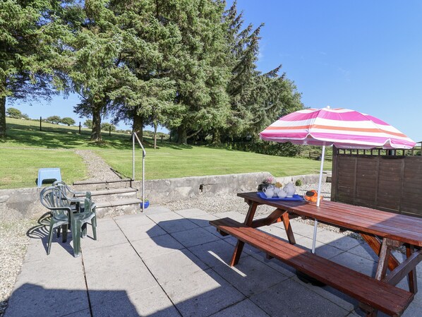 An outdoor patio area with a picnic table, chairs, and a striped umbrella. - The Dairy (Liskeard)