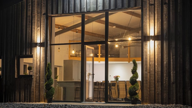 Un edificio moderno con amplios ventanales de vidrio, fachada de madera y un interior visible que incluye un comedor.