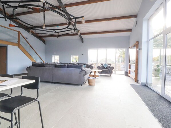 A spacious living area with a large gray sofa, a dining table with chairs, and a staircase leading to an upper level. - The Old Sheep House (Settle)