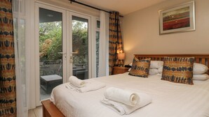 A hotel room with a large bed, a bedside table with a lamp, and a view of the outdoors through a sliding glass door. - Blue Hill House (Ambleside)