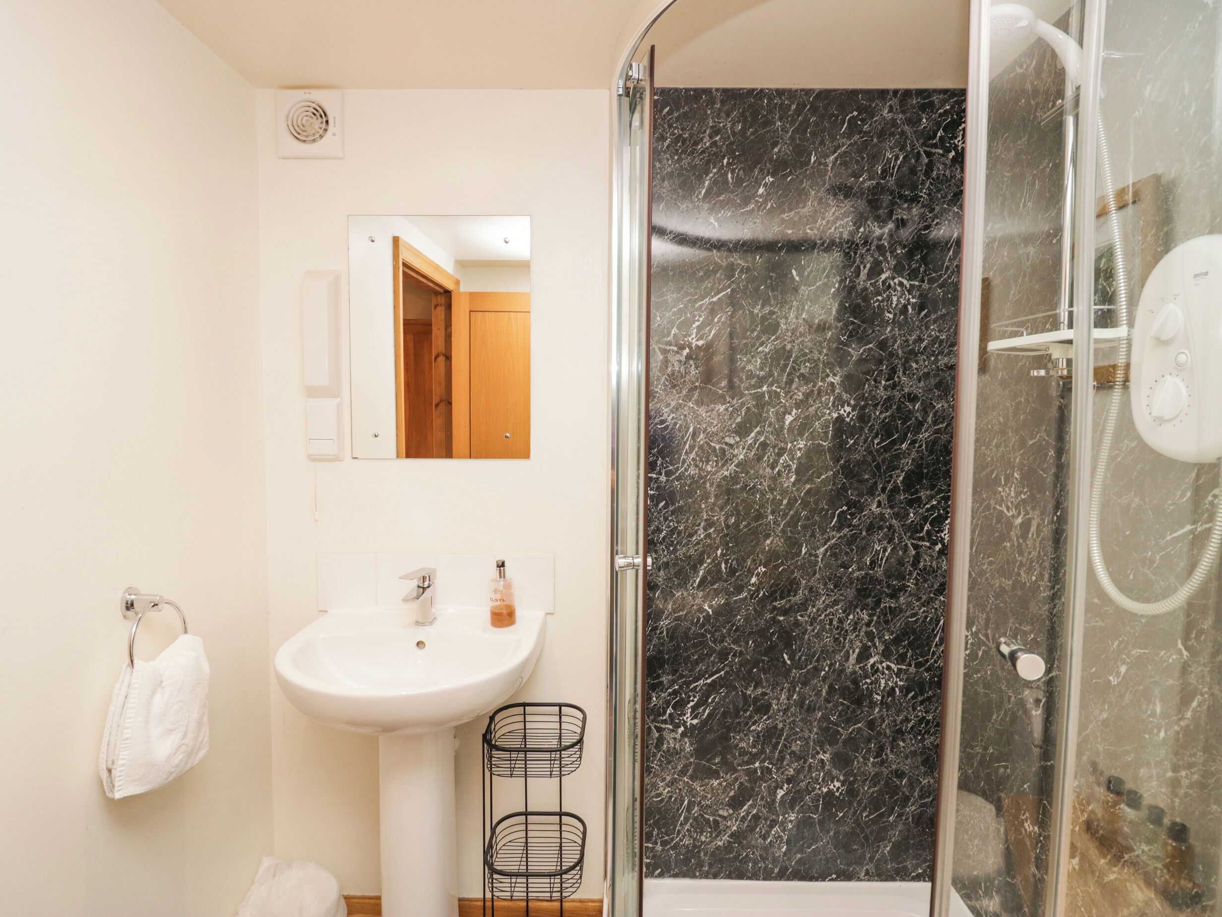 Une salle de bain avec un lavabo blanc, un miroir, une douche avec une porte en verre et un porte-serviettes.