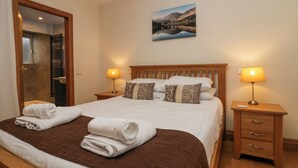 A neatly made bed with a brown headboard, two bedside lamps, and a painting of a landscape on the wall. - Blue Hill House (Ambleside)