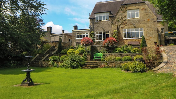 A stone house with a well-maintained garden, a staircase leading to the entrance, and a bench in the garden. - The Old Coach House (Buxton)