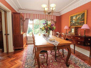 A dining room with a wooden table, chairs, a vase of flowers, and a painting on the wall. - The Old Coach House (Buxton)
