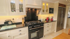 A modern kitchen with white cabinetry, a black stove, and a stainless steel refrigerator. - The Old Coach House (Buxton)