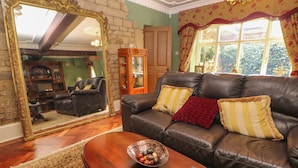 A cozy living room with a leather sofa, a wooden coffee table, and a large mirror. - The Old Coach House (Buxton)