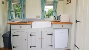 A compact kitchen with a wooden countertop, white appliances, and teal curtains.