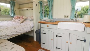 A cozy bedroom with a bed, a small kitchenette, and a window with curtains.