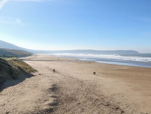 A wide sandy beach with gentle waves, a clear sky, and distant hills. - Cuckoo's Nest (Barnstaple)