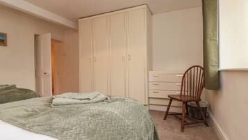 A bedroom with a bed, a wardrobe, a chair, and a door leading to another room.