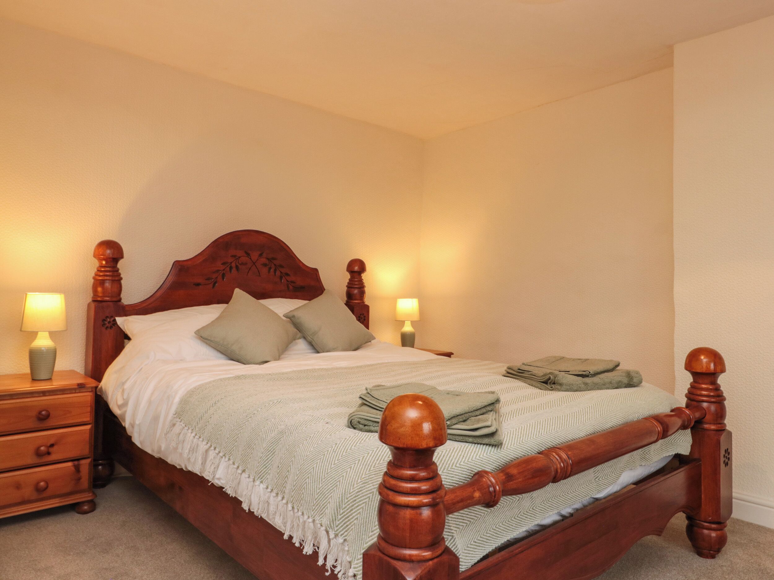 A wooden four-poster bed with two nightstands, each with a lamp.