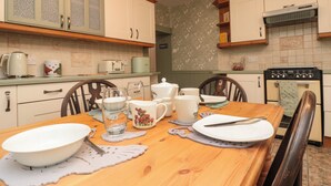 Una cocina con una mesa de madera dispuesta para comer, equipada con fuentes, platos y cubiertos.