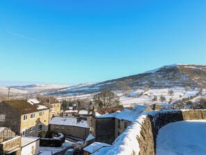 A historic stone building with a courtyard, surrounded by snow-covered fields and a hill in the background.
