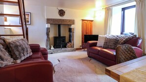 A cozy living room with a fireplace, leather sofas, a wooden table, and a television. - Peak Cottage (Hope Valley)