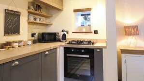 A modern kitchen with a microwave, stove, oven, and wooden shelves. - Peak Cottage (Hope Valley)