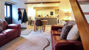 A cozy living room with a fireplace, a dining area, and a kitchen in the background. - Peak Cottage (Hope Valley)