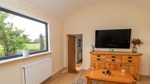 A room with a large window, a wooden cabinet, a television, and a table with decorative items. - The View (Wrexham)
