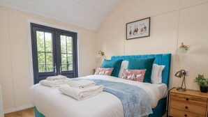 A neatly made bed with a teal headboard, white bedding, and a blue throw blanket. There are two bedside tables with lamps and a framed picture on the wall. - The View (Wrexham)