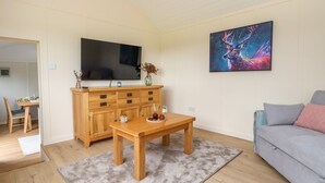 A living room with a wooden cabinet, a television, a painting, a sofa, and a dining table. - The View (Wrexham)