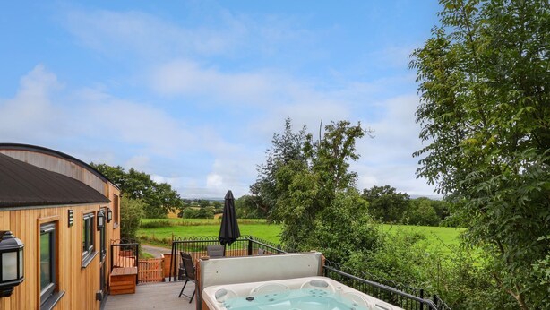 A wooden deck with a hot tub, outdoor seating, and a view of a green landscape. - The View (Wrexham)