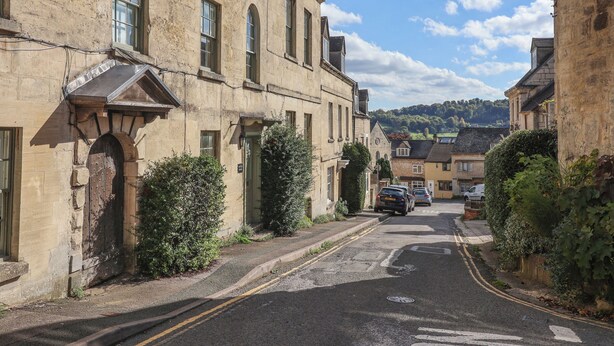 A narrow street lined with historic stone buildings, featuring arched windows and a traditional facade. - Highgrove Barn (Stroud)